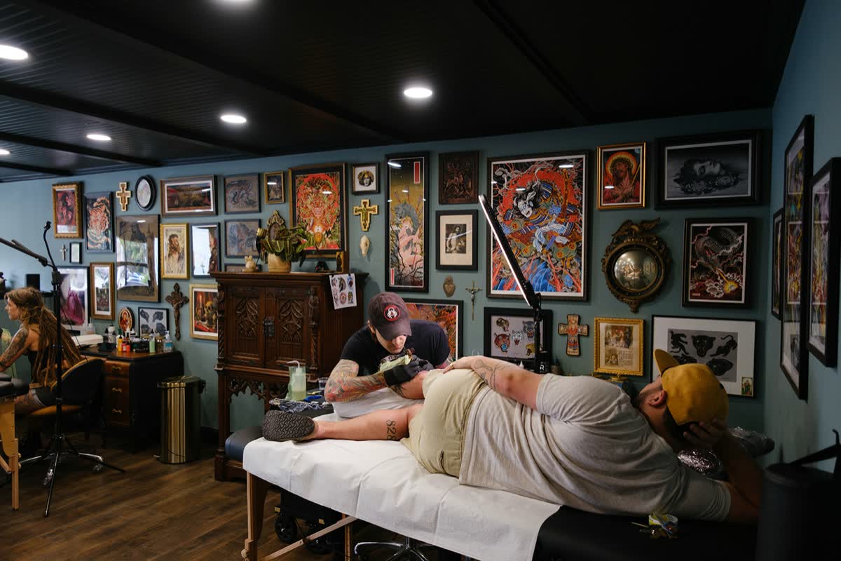 Christopher Cousins tattooing beneath the studio's gallery wall