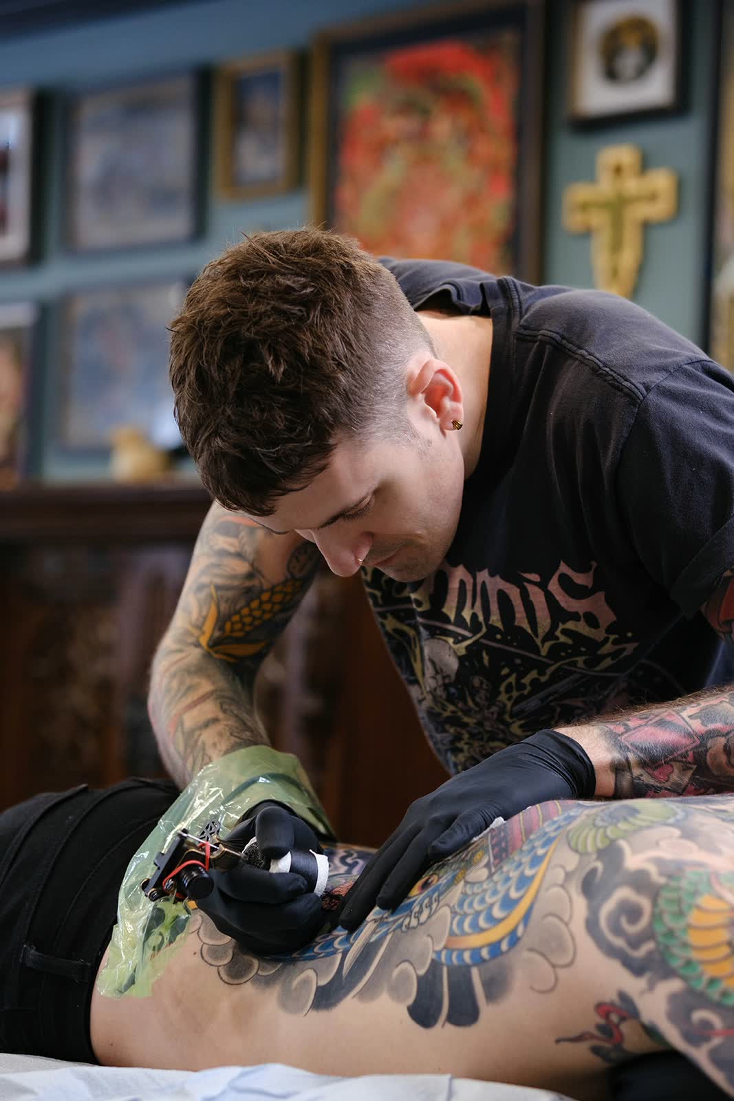 Christopher Cousins tattooing a back piece beneath the studio's gallery wall